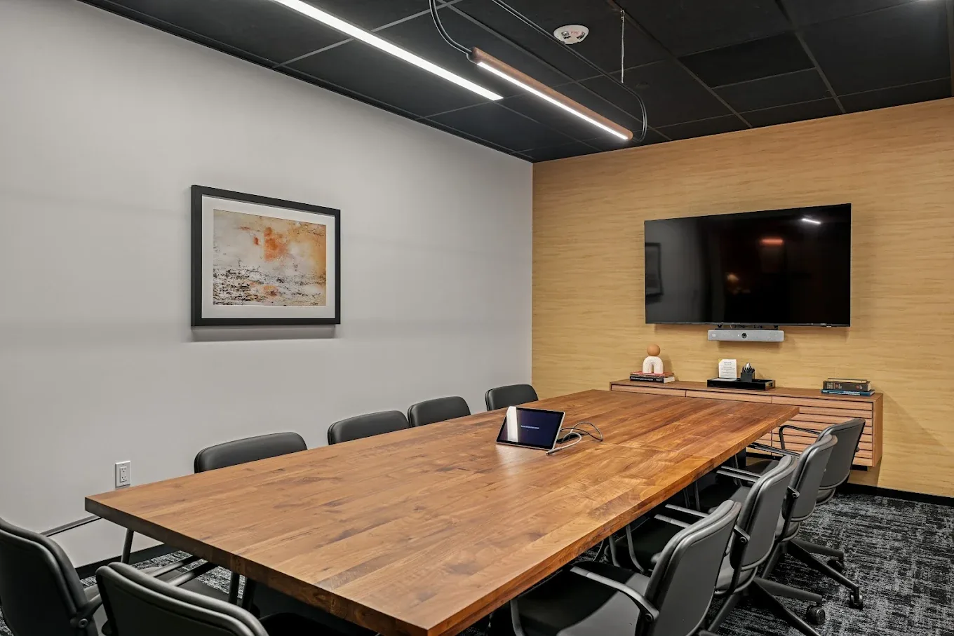 A boardroom with a long walnut table, black chairs and a wall-mounted screen
