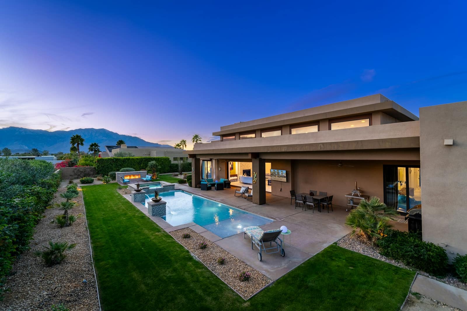 Modern home with a pool and lawn at dusk