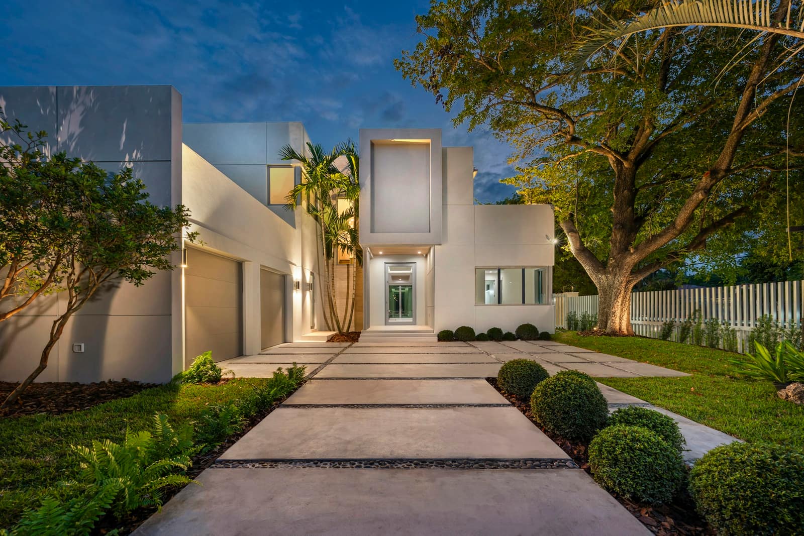 Modern white home with a lit pathway at dusk